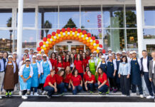 Conad Adriatico rafforza la rete marchigiana con un format evoluto nel Piceno Group of staff and managers posing in front of a store entrance under a colorful balloon arch (red, yellow, orange) for a celebration event.