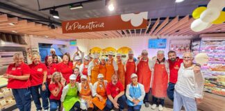Group of bakery employees in red shirts and aprons posing together inside a La Panetteria shop.