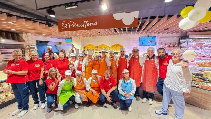 Conad Sulmona (1) Group of bakery employees in red shirts and aprons posing together inside a La Panetteria shop.