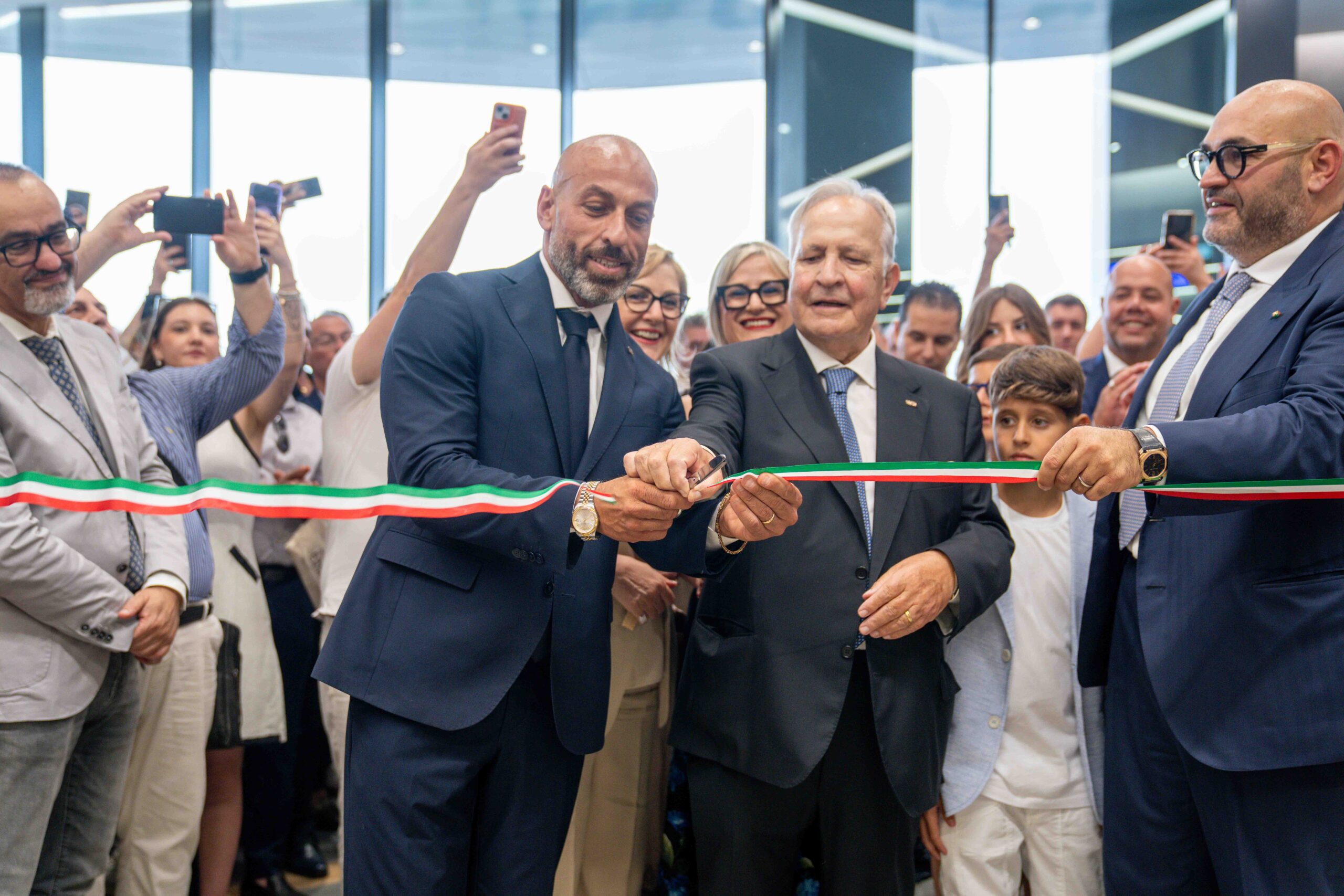 Officials cut a tri-color ribbon at a ceremony while a crowd takes photos.