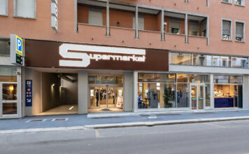 Esselunga riapre lo storico supermercato di viale Piave a Milano Brown storefront with large white 'S' logo and 'Supermarkt' sign; glass entrance with people inside, blue parking sign on left outside.
