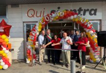 Group of people cutting a ribbon at a store opening under a colorful balloon arch outside the entrance