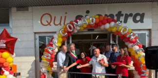 Group of people cutting a ribbon at a store opening under a colorful balloon arch outside the entrance