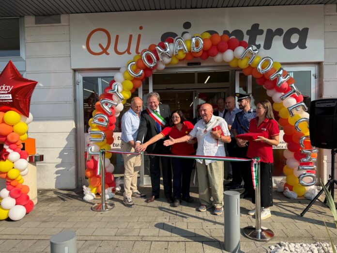 Group of people cutting a ribbon at a store opening under a colorful balloon arch outside the entrance