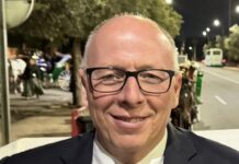 Smiling man in a dark suit and red patterned tie, wearing glasses, at night on a street.