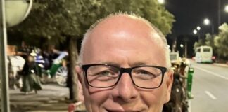 Cambio al vertice di Forum: termina l’incarico di Enrico Fattori Smiling man in a dark suit and red patterned tie, wearing glasses, at night on a street.