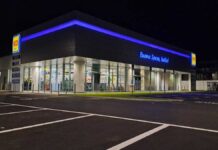 Nighttime view of a modern MD supermarket with blue neon lighting and glass entrance, Italian slogan reading 'Buona Spesa, Italia!'