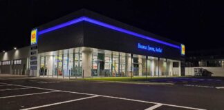 MD apre nel Salernitano e porta a 115 i punti vendita in Campania Nighttime view of a modern MD supermarket with blue neon lighting and glass entrance, Italian slogan reading 'Buona Spesa, Italia!'