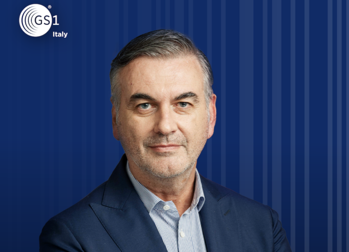 Francesco Avanzini_GS1 Italy Francesco Avanzini, Presidente GS1 Italy, portrait in a navy suit against a blue striped backdrop with the GS1 Italy logo