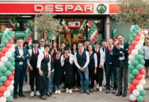 Group of Spar staff posing outside the store, wearing uniforms, with green, white and red balloon arches for a festive event.