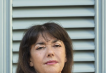 Portrait of a middle-aged woman with dark hair in a red blazer standing in front of a gray vented wall.