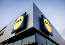 Lidl Italia conquista oltre un milione di nuove famiglie in 13 mesi Exterior of a Lidl store with large round yellow and blue logos on a gray, modern building against a blue sky