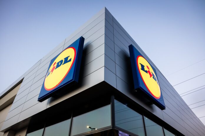 Lidl_foto Exterior of a Lidl store with large round yellow and blue logos on a gray, modern building against a blue sky