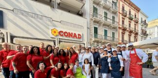 Group of CONAD staff and chefs posing for a photo outside a supermarket on a sunny street.