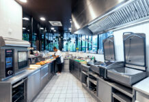 Commercial kitchen with stainless steel appliances; a chef prepares sandwiches on the counter.