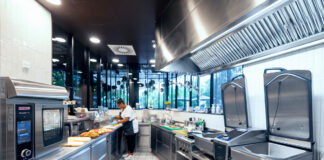 RATIONAL porta il ROI al centro degli investimenti in cucina Commercial kitchen with stainless steel appliances; a chef prepares sandwiches on the counter.