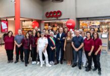 Group of Coop staff and customers posing for a photo outside a supermarket entrance during a store opening, with red balloons and interior visible.