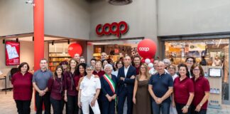 Nova Coop rafforza la rete in provincia di Vercelli con il format Superstore Group of Coop staff and customers posing for a photo outside a supermarket entrance during a store opening, with red balloons and interior visible.