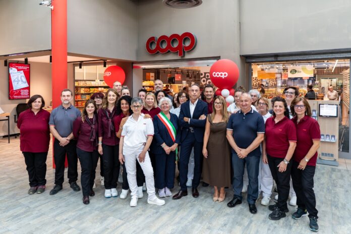 SS_Santhia - Gruppo ingresso negozio Group of Coop staff and customers posing for a photo outside a supermarket entrance during a store opening, with red balloons and interior visible.