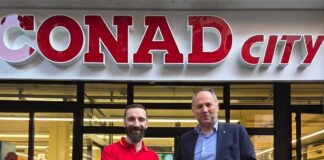 Two men shake hands in front of a CONAD City supermarket storefront