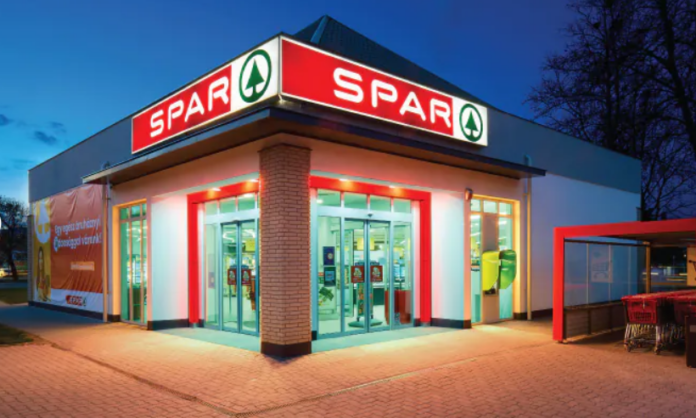 Spar store Exterior view of a SPAR supermarket at dusk with glass automatic doors, red signage, and a brick pillar.