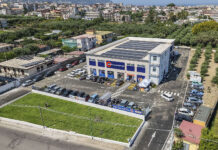Sole365 accelera lo sviluppo in Campania con due nuovi supermercati Aerial view of a two?story retail building with blue storefronts, a parking lot full of cars, and solar panels on the roof