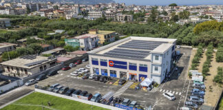 Sole365 accelera lo sviluppo in Campania con due nuovi supermercati Aerial view of a two?story retail building with blue storefronts, a parking lot full of cars, and solar panels on the roof