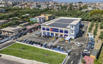 Sole365 accelera lo sviluppo in Campania con due nuovi supermercati Aerial view of a two?story retail building with blue storefronts, a parking lot full of cars, and solar panels on the roof