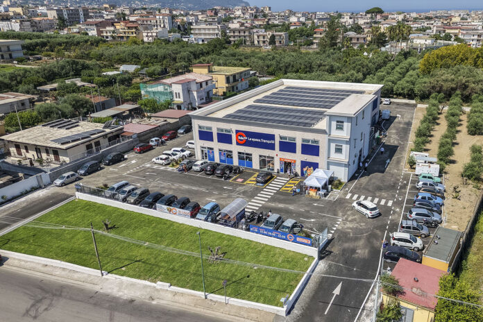 default Aerial view of a two?story retail building with blue storefronts, a parking lot full of cars, and solar panels on the roof