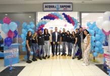 Acqua & Sapone cresce con tre nuove aperture in Liguria, Piemonte e Calabria Staff group posing under a blue-pink balloon arch at Acqua e Sapone store opening ceremony in a shopping center.