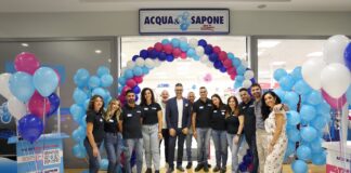 Staff group posing under a blue-pink balloon arch at Acqua e Sapone store opening ceremony in a shopping center.