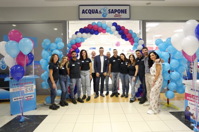 Staff group posing under a blue-pink balloon arch at Acqua e Sapone store opening ceremony in a shopping center.