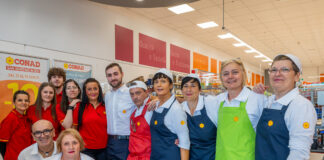 Conad Centro Nord porta l’insegna a San Polo d’Enza e San Martino in Rio Group of CONAD supermarket staff posing for a photo, wearing red shirts and blue or green aprons with yellow flowers.