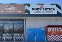 Front of a shopping plaza with Sablé Pasticceria e Caffè and RomAntica La Pizza alla Romana signs, glass doors, and blue Amazon lockers beside red parcel lockers; balloons on the left.