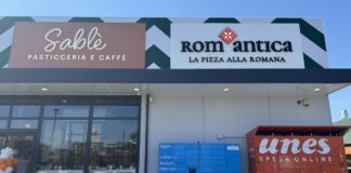 Front of a shopping plaza with Sablé Pasticceria e Caffè and RomAntica La Pizza alla Romana signs, glass doors, and blue Amazon lockers beside red parcel lockers; balloons on the left.