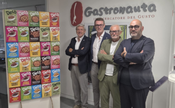 Four men in smart-casual attire pose with crossed arms in front of a wall with the 'Gastronauta' logo and a colorful cereal box display on a stand.