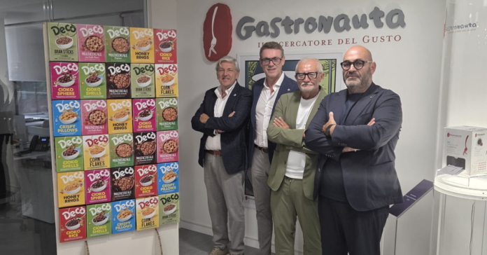 Four men in smart-casual attire pose with crossed arms in front of a wall with the 'Gastronauta' logo and a colorful cereal box display on a stand.