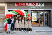 Group of staff in beige aprons posing outside a Despar Express store under a red-green balloon arch.