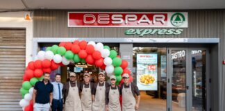 Group of staff in beige aprons posing outside a Despar Express store under a red-green balloon arch.