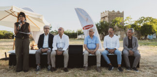Granoro, la filiera del grano duro pugliese diventa racconto di prodotto Outdoor panel discussion with six people seated on a black stage; a woman on the left speaks into a microphone, Granoro banner in the background.