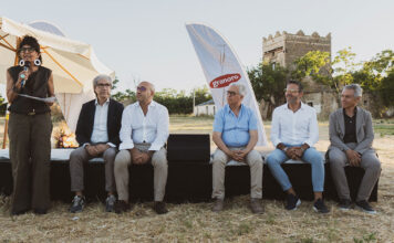 Outdoor panel discussion with six people seated on a black stage; a woman on the left speaks into a microphone, Granoro banner in the background.