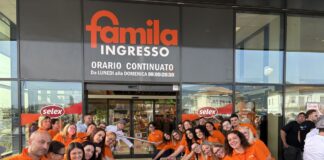 Staff in orange shirts line up at the Famila entrance for a ribbon-cutting ceremony outside the store as onlookers watch the opening.