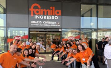 Staff in orange shirts line up at the Famila entrance for a ribbon-cutting ceremony outside the store as onlookers watch the opening.