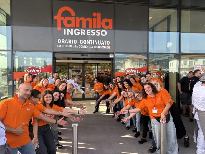 gmf_calcinaia_luglio 2026 (67) Staff in orange shirts line up at the Famila entrance for a ribbon-cutting ceremony outside the store as onlookers watch the opening.