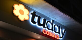 Nighttime exterior sign for a Conad supermarket with a yellow-orange flower logo and the word 'CONAD' in red letters.