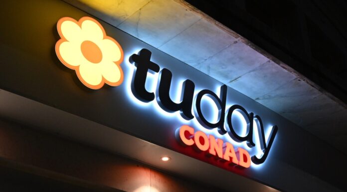 insegna_tuday_conad_generica Nighttime exterior sign for a Conad supermarket with a yellow-orange flower logo and the word 'CONAD' in red letters.