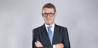 Professional portrait of a man in a dark suit with a blue tie, arms crossed, facing the camera.
