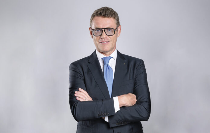Professional portrait of a man in a dark suit with a blue tie, arms crossed, facing the camera.