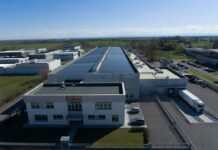 Comal Salumi rafforza il dialogo con retail e filiera attraverso il primo Bilancio ESG Aerial view of a large industrial facility with solar panels on the roof and delivery trucks at a loading dock.