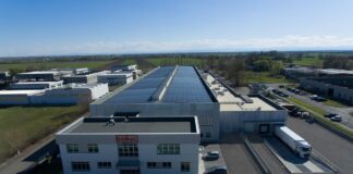 Comal Salumi rafforza il dialogo con retail e filiera attraverso il primo Bilancio ESG Aerial view of a large industrial facility with solar panels on the roof and delivery trucks at a loading dock.